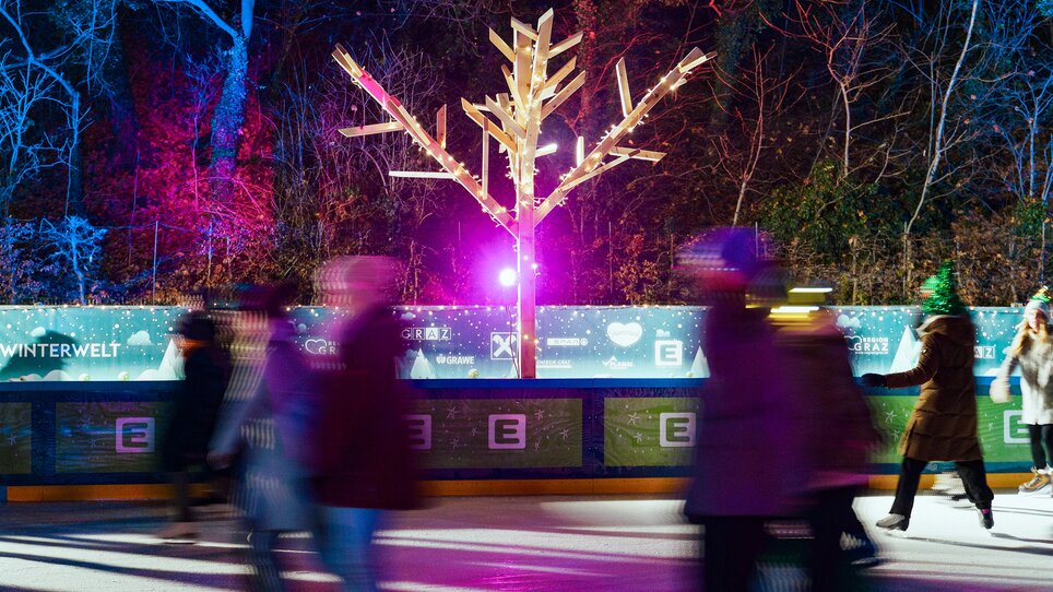 Skaters on a lit rink with a decorated tree. | © Leon Moik