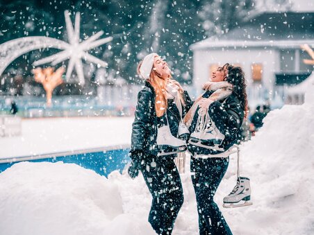 Two women laughing while holding ice skates in a winter wonderland. | © Stefan Leitner