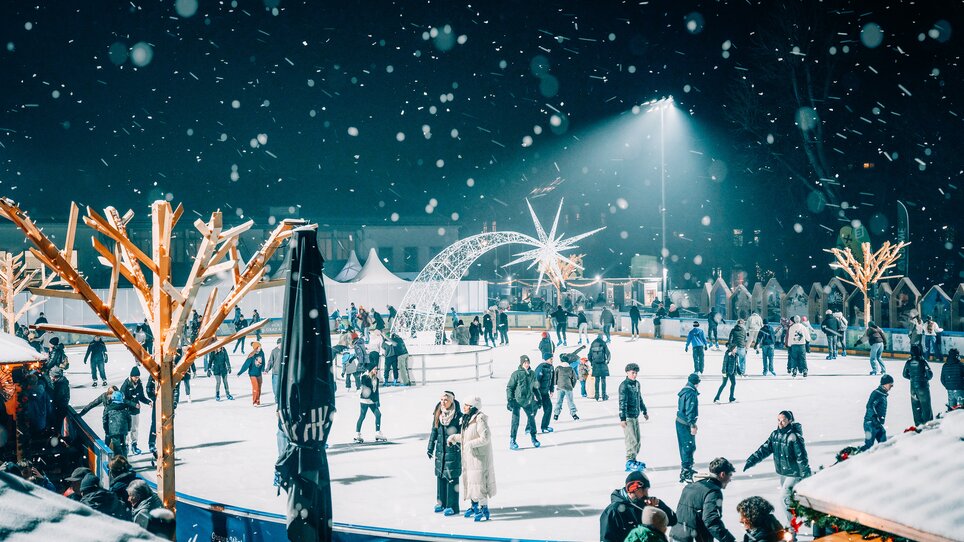 Illuminated ice rink in Graz, surrounded by snow-covered trees and visitors. | © Stefan Leitner