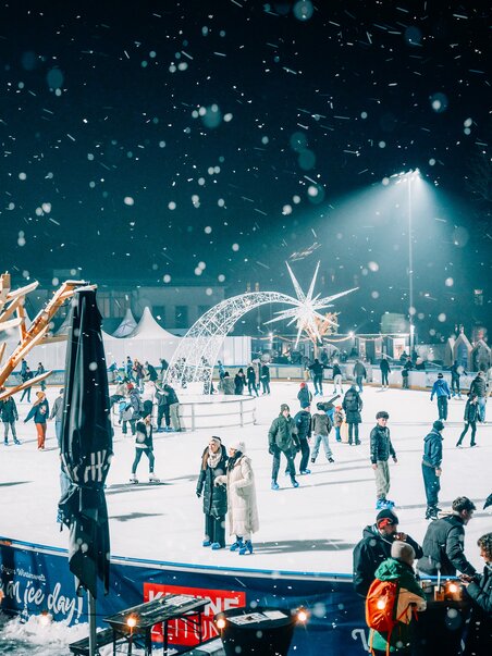 Illuminated ice rink in Graz, surrounded by snow-covered trees and visitors. | © Stefan Leitner
