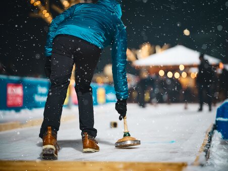 A curling player on a festively decorated ice skating rink. | © Stefan Leitner
