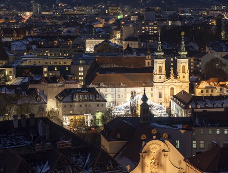 Illuminated city of Graz at night with snow on rooftops and Mariahilferplatz in the foreground. | © Vincent Croce