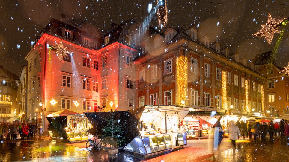 Festliche Atmosphäre mit Weihnachtsständen und Schneefall am Mehlplatz in Graz. | © Graz Tourismus - Harry Schiffer