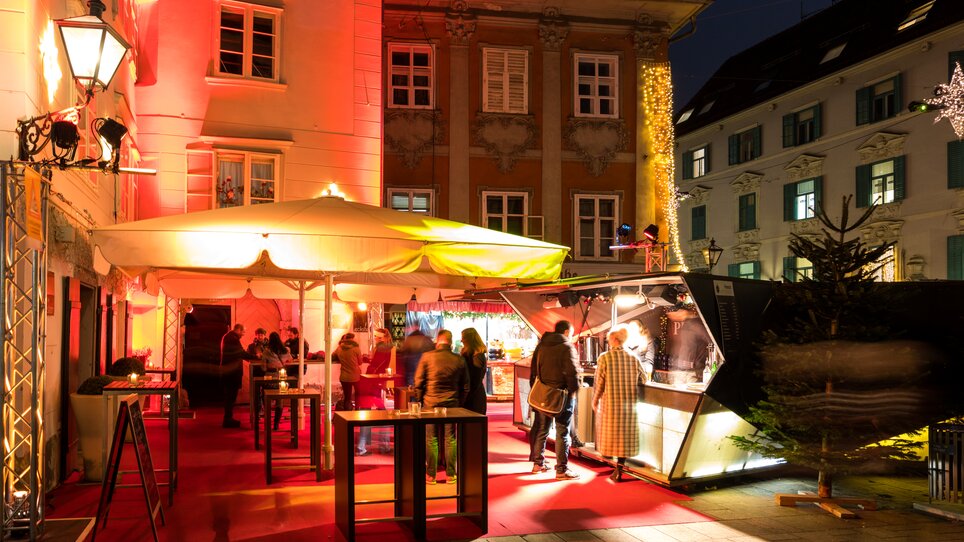 Beleuchteter Adventmarkt am Mehlplatz mit festlicher Dekoration und Besuchern. | © Graz Tourismus - Harry Schiffer