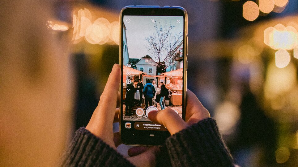 Una persona fotografa un mercatino di Natale con luci e visitatori. | © Evgenia Rieger Photography