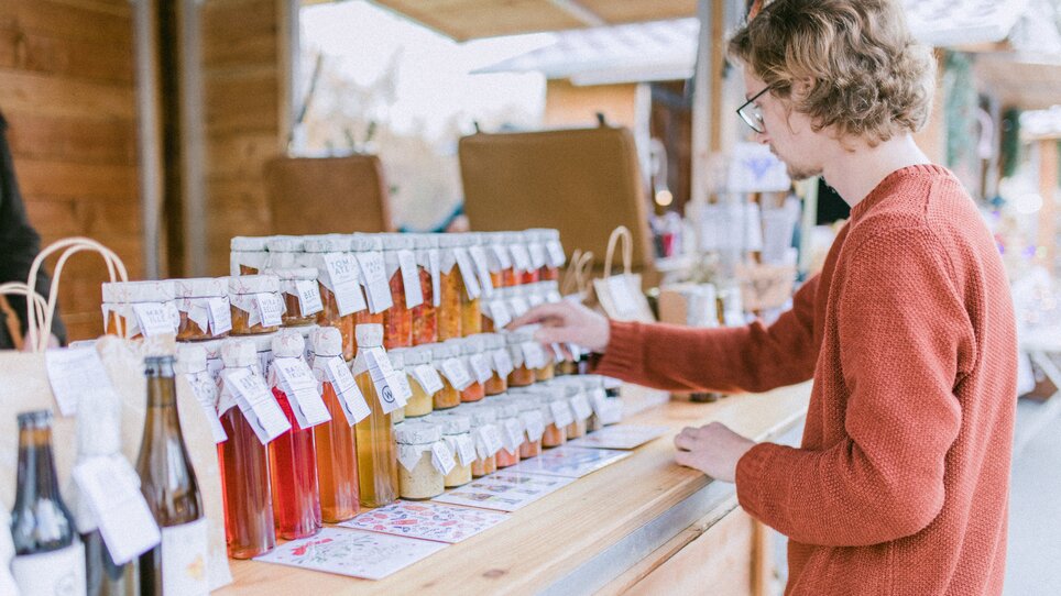 Un giovane osserva una selezione di bottiglie con vari contenuti in un mercatino di Natale. | © Evgenia Rieger Photography
