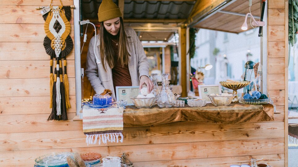 Una donna è a un banco di mercato che vende piatti e articoli decorativi. | © Evgenia Rieger Photography