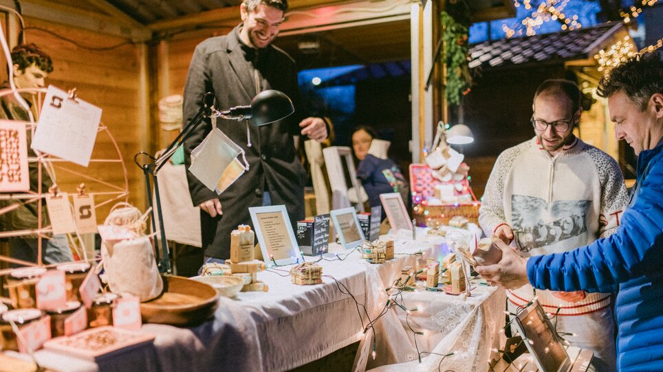 Mercatino di Natale con bancarelle e visitatori, splendidamente illuminato. | © Evgenia Rieger Photography