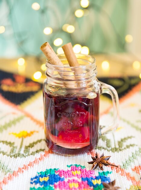A glass of punch, garnished with cinnamon sticks and star anise, with atmospheric lights in the background. | © Evgenia Rieger Photography