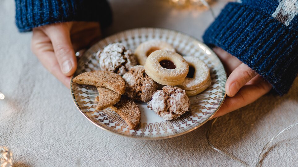 A person holds a plate of assorted cookies in hands, surrounded by lights. | © Evgenia Rieger Photography