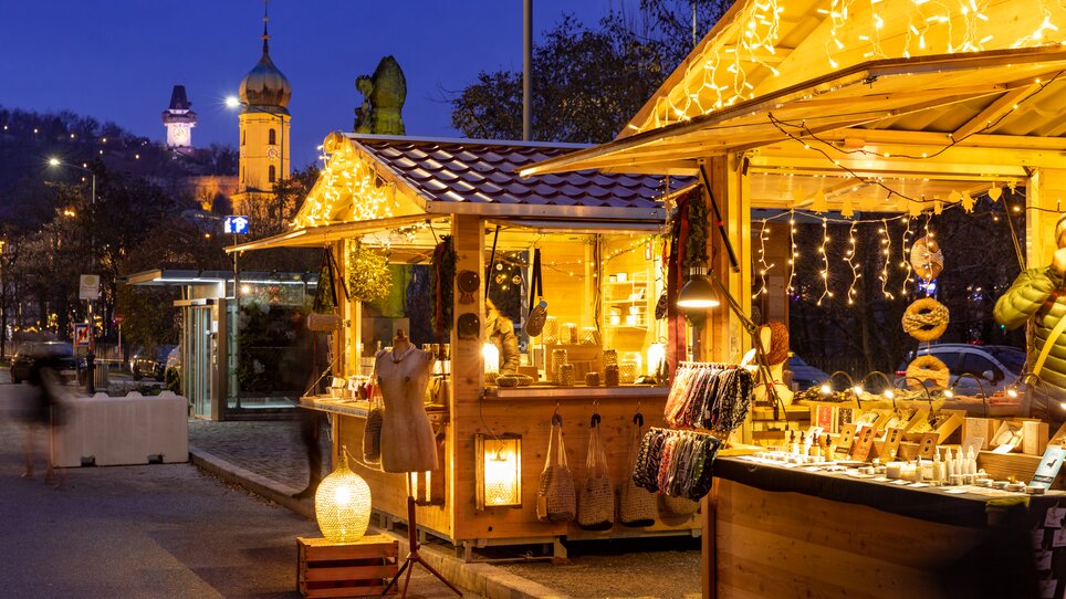 Beleuchtete Weihnachtsmarktstände mit Dekoration und Produkten in Graz. | © Graz Tourismus - Harry Schiffer