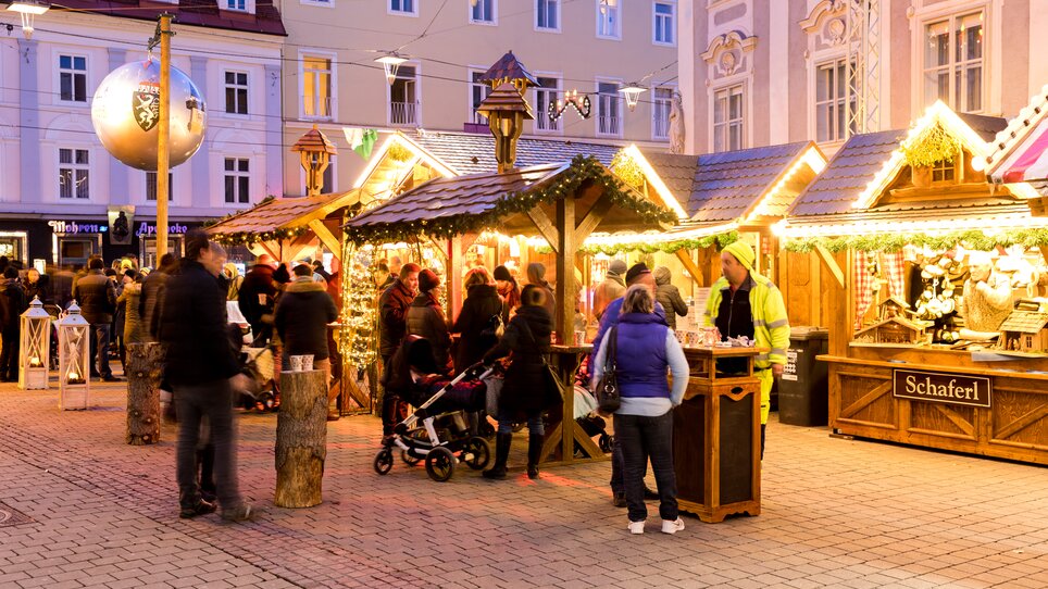 Belebte Szene am Christkindlmarkt in Graz mit festlich dekorierten Holzständen und Besuchern. | © Graz Tourismus - Harry Schiffer