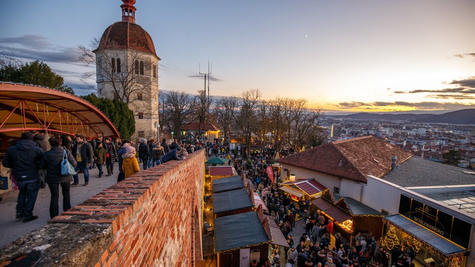 Advent in Graz I “Aufsteirern”-Christmas market on Schlossberg hill | © ivents - Erwin Scheriau View of the Christmas market on Schlossberg in Graz with many people and a stunning sunset in the background. | © ivents - Erwin Scheriau