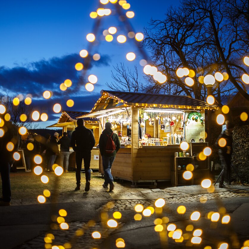 Weihnachtsmarkt mit bunten Lichtern und Ständen, unter blauem Himmel. | © ivents - Erwin Scheriau