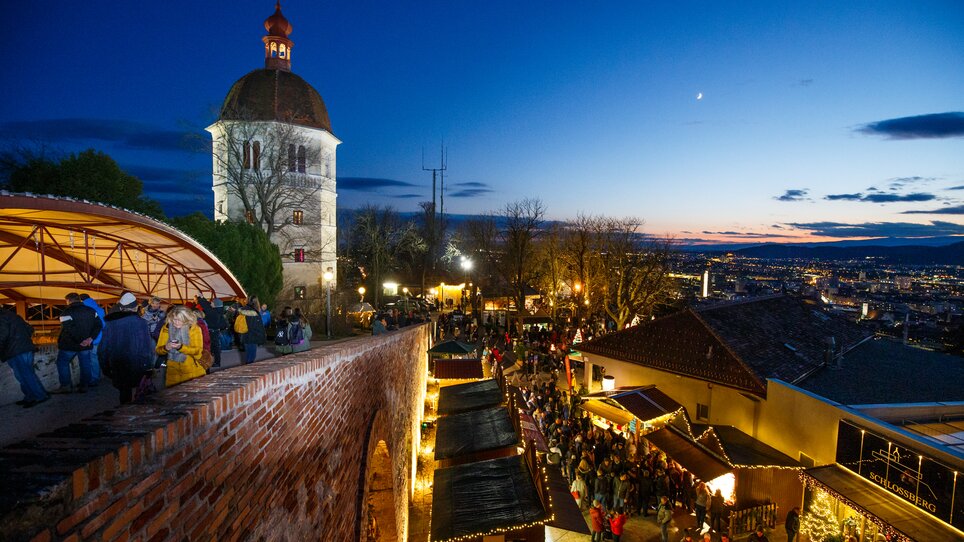 Advent in Graz I “Aufsteirern”-Christmas market on Schlossberg hill | © ivents - Erwin Scheriau View of the Graz Bell Tower, Christmas market stalls, and the city of Graz in the evening light. | © ivents - Erwin Scheriau