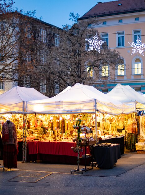 A festive Advent market scene with brightly lit stalls and people in Graz. | © Graz Tourismus - Harry Schiffer