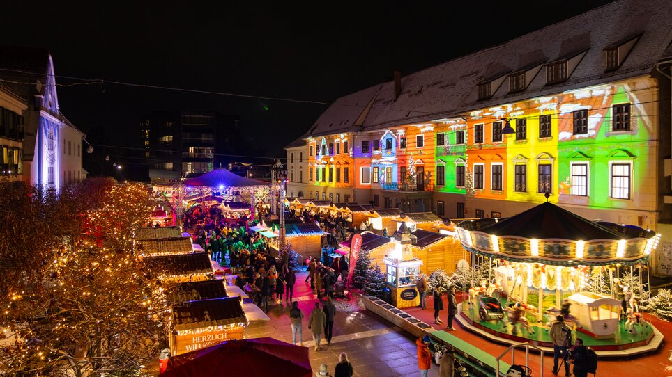 Beleuchteter Weihnachtsmarkt in Graz mit festlichen Ständen und Karussell. | © Harry Schiffer