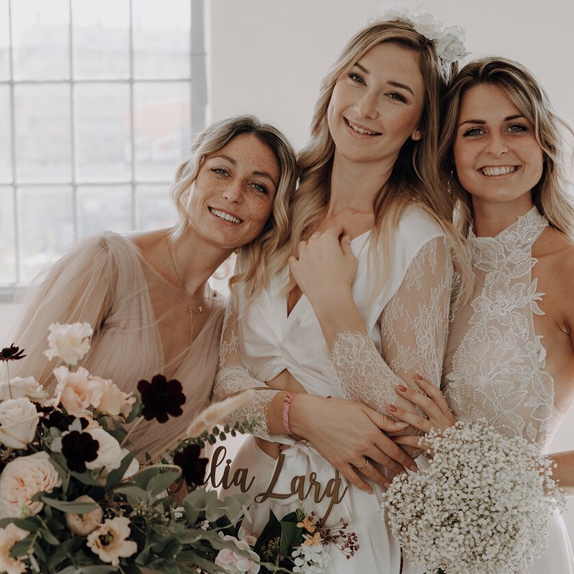 Drei junge Frauen in Brautkleidern lächeln in die Kamera | © THE CLICK Wedding
