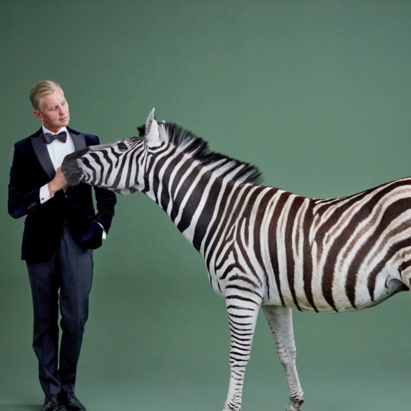 Ein Mann in Anzug steht neben einem Zebra vor grünem Hintergrund. | © Max Raabe und Palast Orchester_Gregor Hohenberg