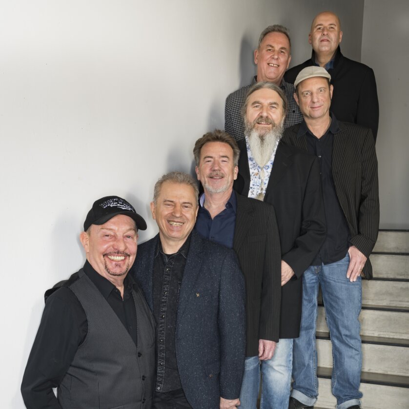 Sechs Männer der Musikgruppe Spider Murphy Gang stehen auf einer Treppe und lächeln in die Kamera. | © Hangen Photo