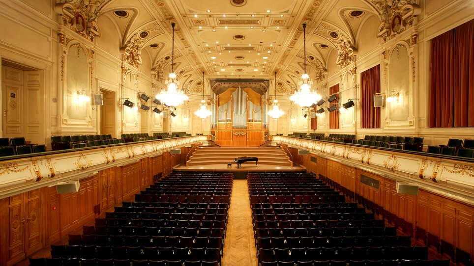 Blick in den Stefaniensaal mit Bestuhlung, Bühne und Decke, die reich mit Stuck verziert ist. | © Illemann