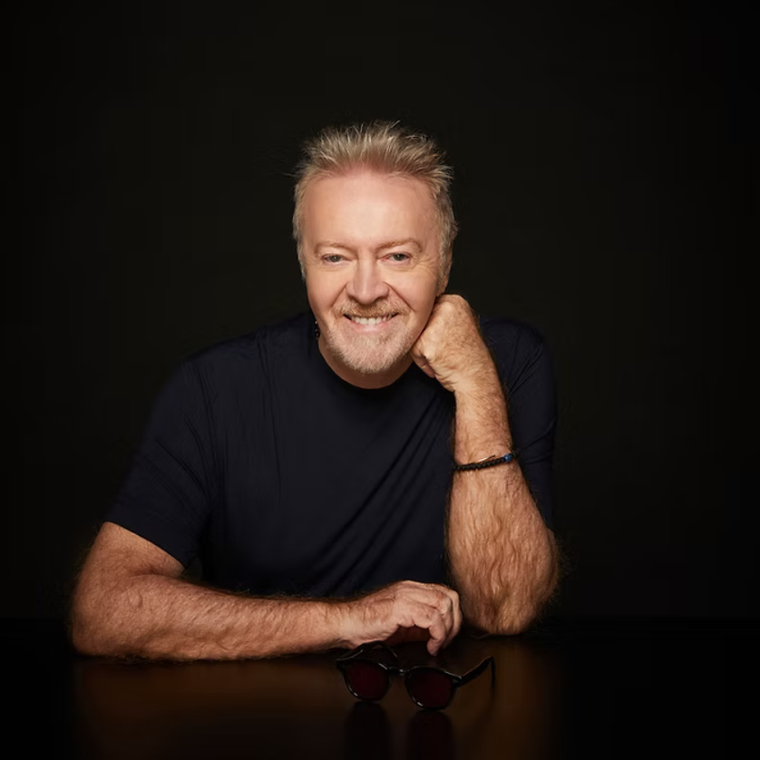 Umberto Tozzi sitzt am Tisch mit einer Hand am Kinn und trägt ein schwarzes T-Shirt. | © Umberto Tozzi