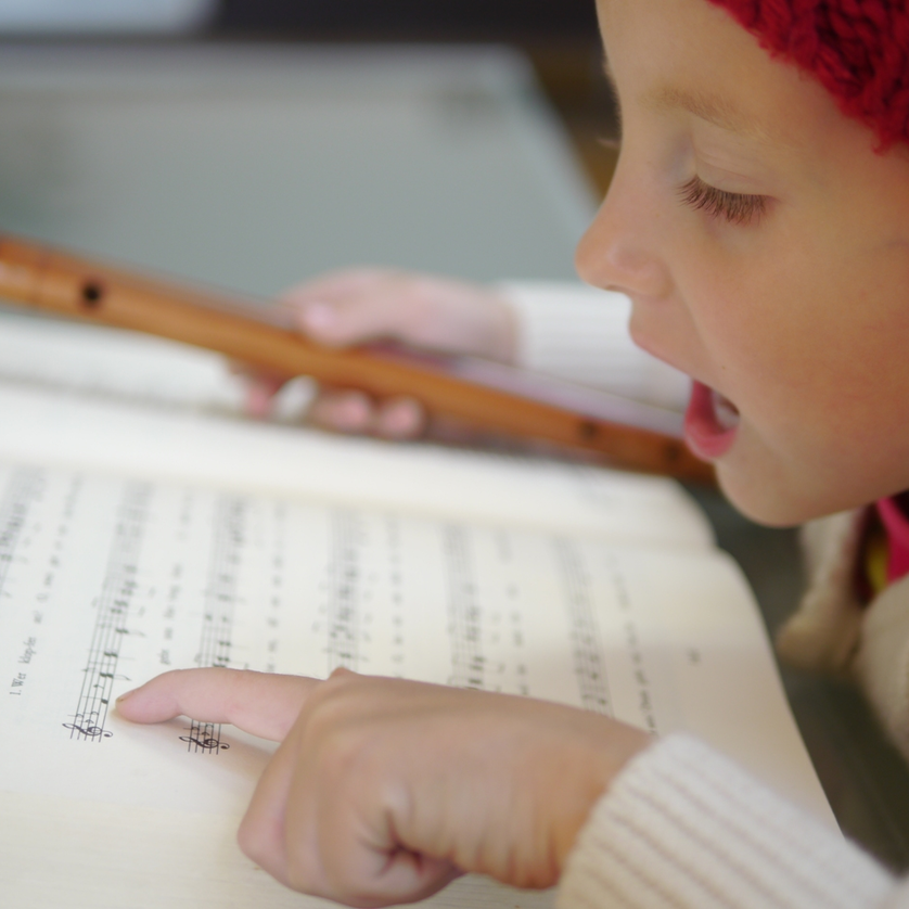 Advent in Graz I Büro für Weihnachtslieder | © Steirisches Volksliedwerk Ein Mädchen mit roter Mütze singt und spielt Flöte, während sie auf Notenblätter schaut. | © Steirisches Volksliedwerk