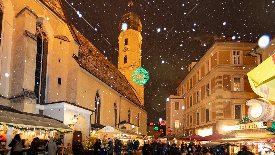 Snow falls over the Christmas market in the Franziskanerviertel in Graz, featuring illuminated stalls and impressive architecture. | © Graz Tourismus-Harry Schiffer