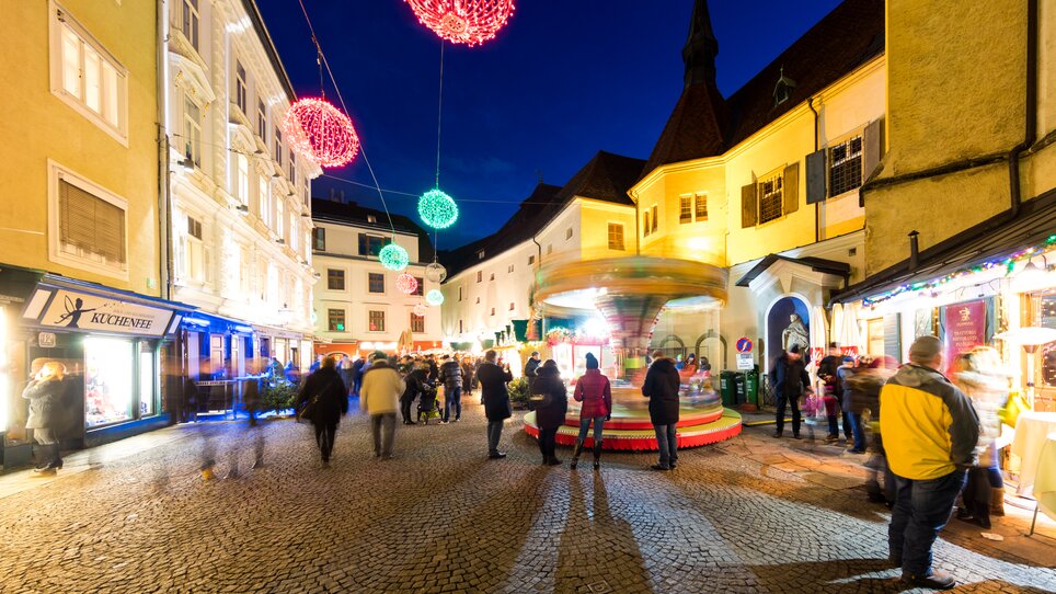 Busy streets adorned with lights, a carousel, and stalls at the Christmas market in Graz. | © Graz Tourismus - Harry Schiffer