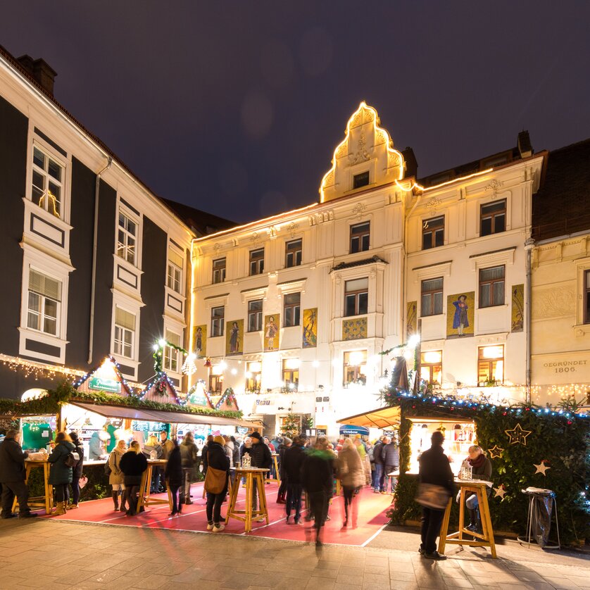 Beleuchteter Adventmarkt am Glockenspielplatz in Graz mit Ständen und Besuchern. | © Graz Tourismus - Harry Schiffer