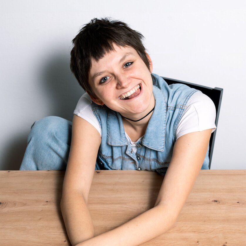 Young person with short hair sitting at a table, smiling. | © Jasmin Pebal