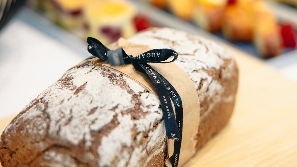 A loaf of brown bread decorated with a bow and the Augarten Art Hotel logo | © Augartenhotel x einsnullneun