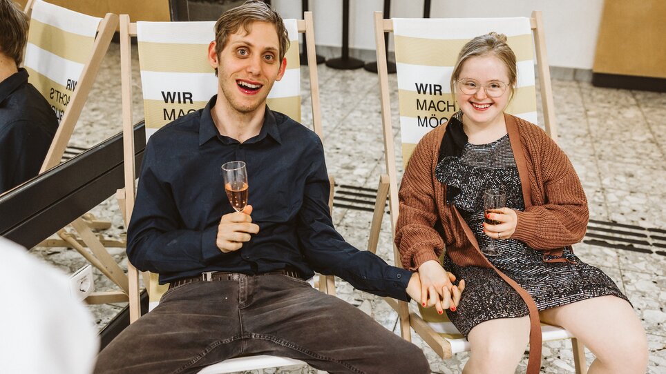 Zwei Personen sitzen und halten Händchen, lächeln, mit Getränken. | © Mario Sudy