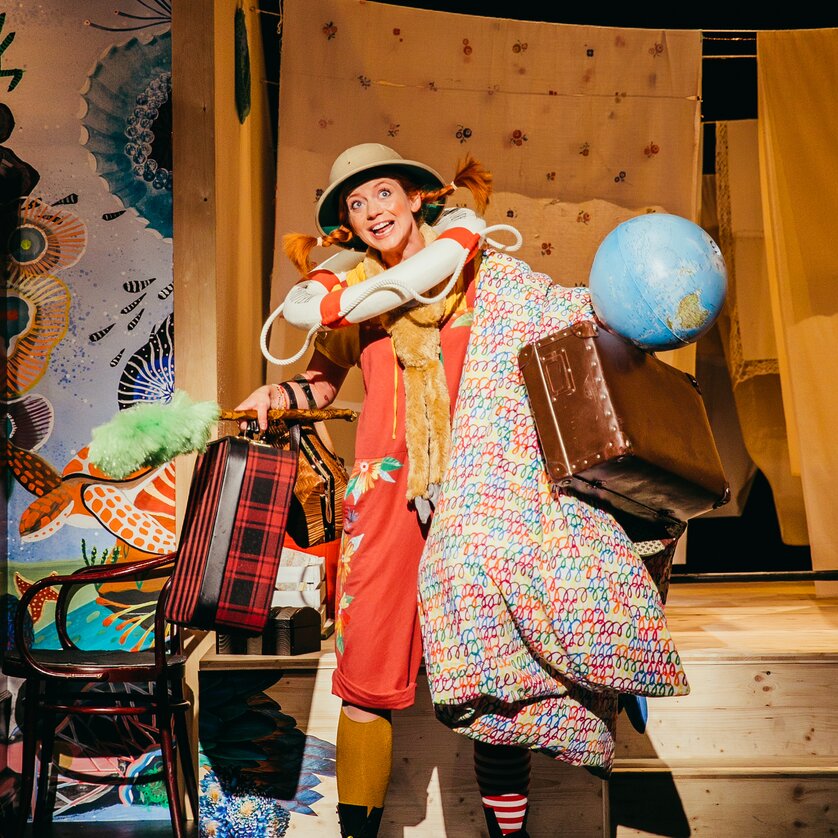 Ein fröhlicher Clown trägt viel Gepäck und einen Globus auf der Bühne. | © Stella