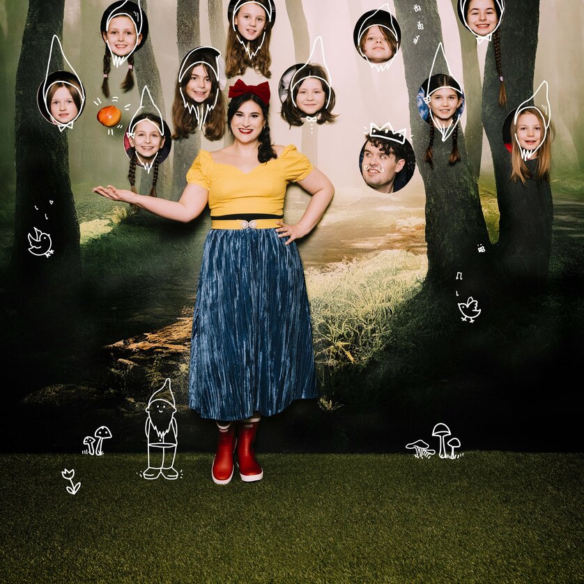 Schneewittchen-und-die-77-Zwerge-Corina-Koller-und-Kinder-der-Singschul | © Oper Graz - Ingo Pertramer Frau als Schneewittchen mit Kindern als Zwerge vor Waldkulisse mit gezeichneten Elementen | © Oper Graz - Ingo Pertramer