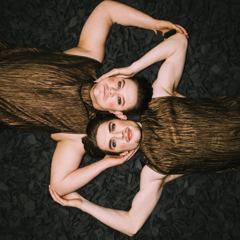 Zwei Personen in bronzefarbenen Outfits liegen auf schwarzem Material. | © Oper Graz - Ingo-Pertramer