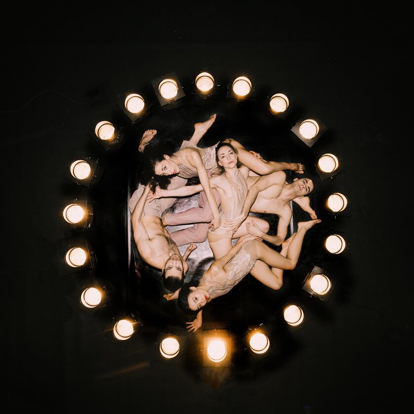 Ring Ballett Graz | © Oper Graz - Ingo Pertramer Fünf Tänzer:innen liegen kreisförmig unter Bühnenlichtern auf dunklem Hintergrund | © Oper Graz - Ingo Pertramer