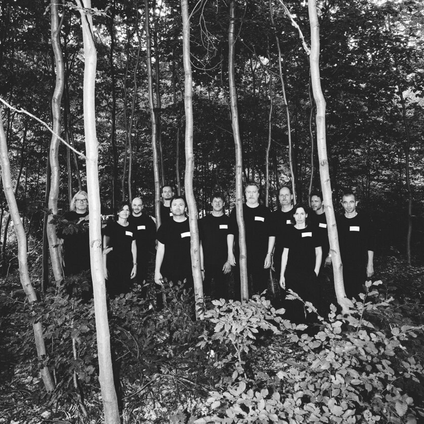 Holzfällen | © Oper Graz - Ingo Pertramer Gruppe in schwarzen Outfits steht still zwischen Bäumen in einem Wald, Schwarz-Weiß-Foto | © Oper Graz - Ingo Pertramer