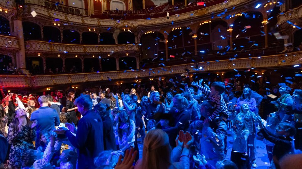 Crowd in a theater catching confetti during a celebration.