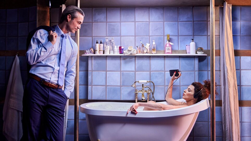 Ein Mann schaut auf eine Frau, die in der Badewanne sitzt und einen Walkman hält. | © William Rutten