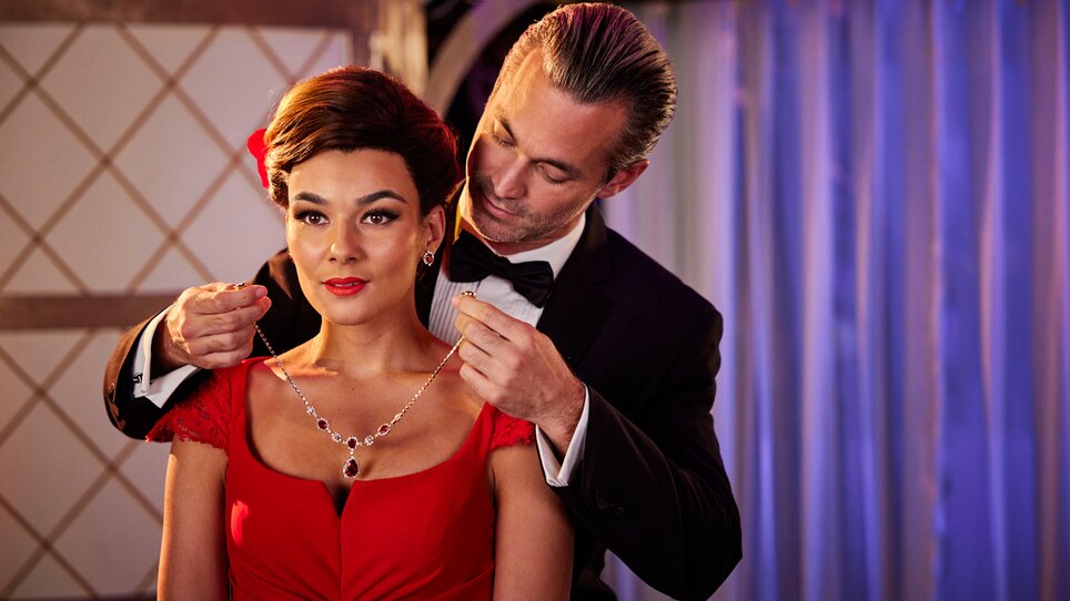 Ein Mann legt einer Frau eine Halskette an, die ein rotes Kleid trägt. | © William Rutten