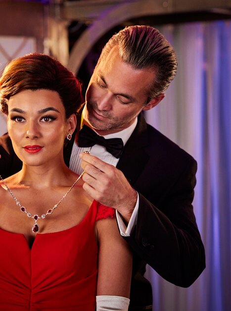 A man puts a necklace on a woman wearing a red dress. | © William Rutten