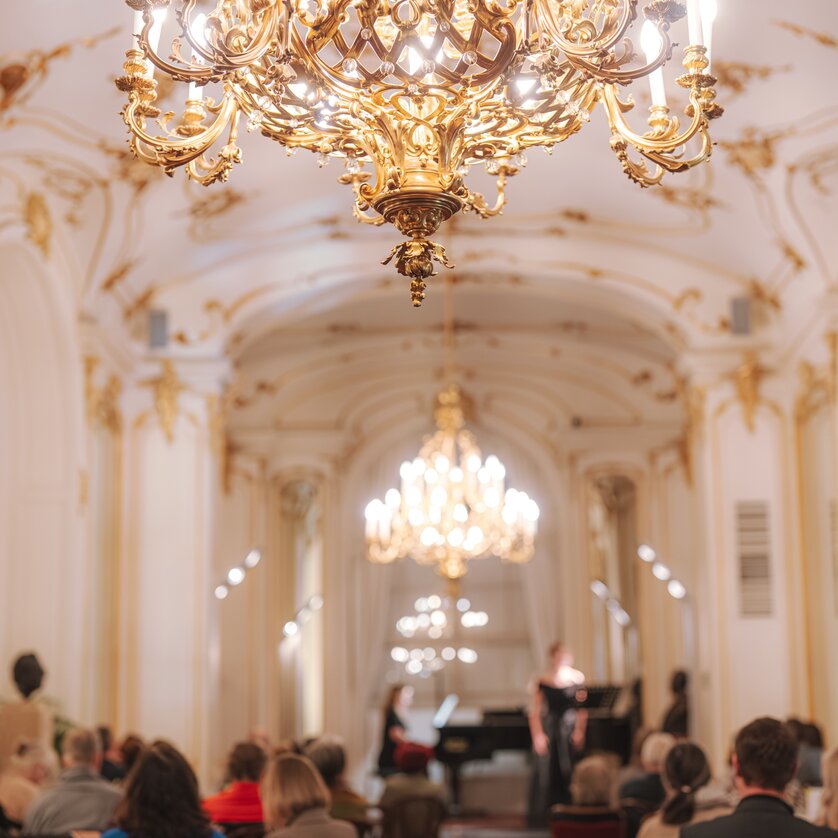 Elegant concert with piano and audience under a chandelier. | © Reithofer Media - Oper Graz