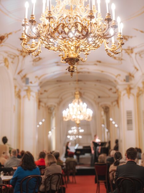 Elegant concert with piano and audience under a chandelier. | © Reithofer Media - Oper Graz
