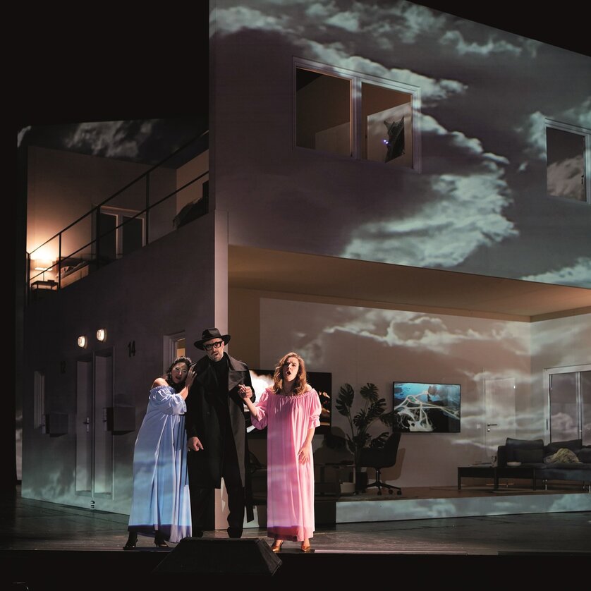Three performers in costumes stand in front of a projected house. | © Reinhard Winkler