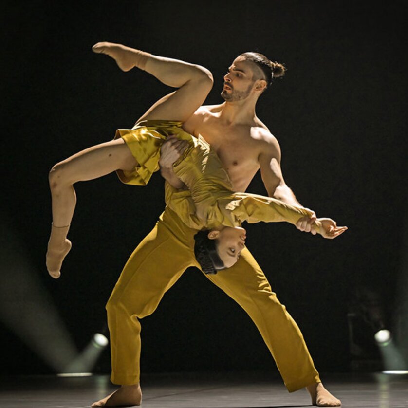 Two dancers in yellow costumes performing a dynamic lift on stage. | © Andreas J. Etter - Oper Graz