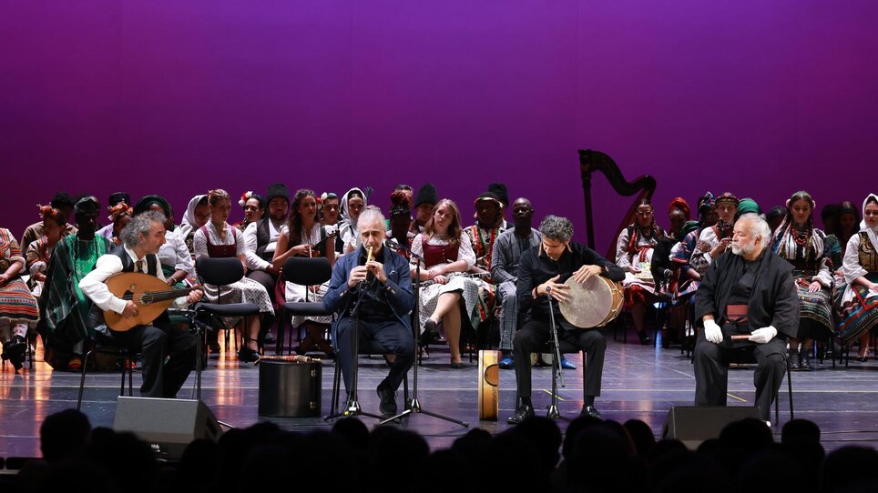 Bühne mit Musikern und einem Chor in traditioneller Kleidung. | © Oliver Wolf