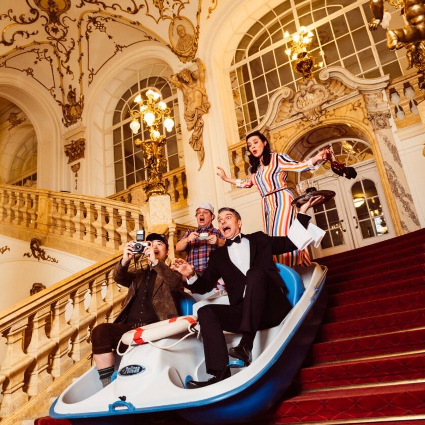 Vier Personen in einem Boot auf einer Treppe in einem prunkvollen Gebäude. | © Ingo Pertramer - Oper Graz