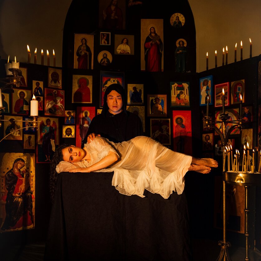 A mystical scene featuring a woman in white and a priest, surrounded by candles and icons. | © Ingo-Pertramer-Oper-Graz