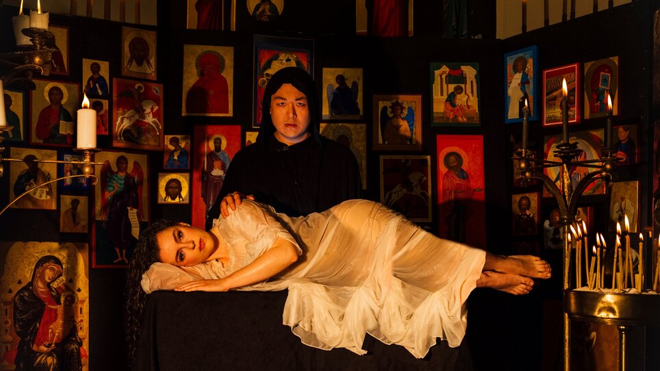 Una scena mistica con una donna in bianco e un sacerdote, circondati da candele e icone. | © Ingo-Pertramer-Oper-Graz